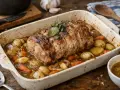 Un savoureux roti de porc au four, doré et juteux, mijotant avec des pommes de terre et des carottes dans un plat en céramique.