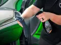Person sprayar en trasa med en produkt för bilvård, en effektiv wax remover, för att rengöra bilens interiör.