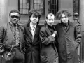 Vier Männer in dunkler Kleidung, Post-Punk-Ästhetik, stehen vor einem Gebäude.