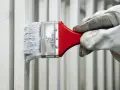Mano guantata stende vernice all'acqua bianca su una ringhiera metallica.