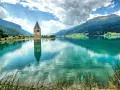 Il lago del campanile, con la sua torre sommersa, riflette montagne verdi e un cielo nuvoloso.