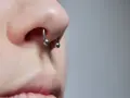 Zbliżenie na nos z kolczykiem typu septril piercing. Metalowy okrąg z dwoma kulkami subtelnie zdobi przegrodę nosową.