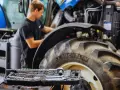 Mechanik pracuje przy traktorze, a obok leży walizka z narzędziami. Kluczowe dla sprawnej konserwacji maszyn rolniczych są regularne przeglądy.