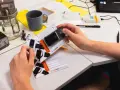 Dłoń trzyma alkomat i certyfikat kalibracji na biurku z przyrządami laboratoryjnymi.