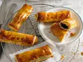 Goldbraune, knusprige Pain au Chocolat auf einem Gitter, einige auf einem Teller, einer aufgeschnitten.
