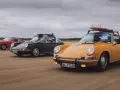 Trzy klasyczne Porsche jadące po plaży. Zdjecie w ruchu, z deskami surfingowymi na dachu jednego z nich.