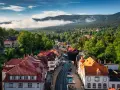 Widok na Szklarską Porębę Rynek z górami w tle. Urokliwe kamienice z czerwonymi dachami w otoczeniu zieleni.