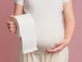 Ciężarna kobieta trzymająca rolkę papieru toaletowego, symbolizująca luźne stolce w ciąży w 1 trymestrze.