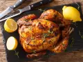 Pollo al horno dorado y jugoso, adornado con tomillo fresco y acompañado de limones cortados. Un festín listo para servir.