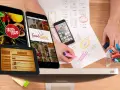 Diseño de apps para restaurantes: teléfonos y tabletas muestran menús y logos. Bocetos y marcadores sugieren planificación.