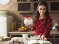 Junge Frau liest Rezept und hält Mehl bereit. Sie überlegt, ob sie Wasser statt Milch beim Backen verwenden soll.