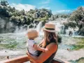 Mama z dzieckiem podziwia wodospady w parku Krka w Chorwacji. Woda jest krystalicznie czysta, a wokół bujna zieleń.
