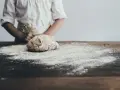Dziecko w fartuszku przygotowuje masę solną. Na drewnianym stole rozsypana mąka, idealna do lepienia.