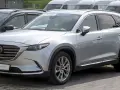 Srebrna Mazda CX-9 z napisem "PRE-OWNED" na przedniej szybie, zaparkowana na zewnątrz.
