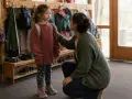 Ein Elternteil tröstet ein Kind, das mit Rucksack und Jacke bereitsteht. Die Kinder Trennung Eltern ist ein emotionaler Moment.