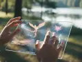 Ręce trzymają przezroczysty tablet, na którym **Adobe Firefly** tworzy magiczne, świetliste stworzenia, jak ptak i ważki, na tle natury.