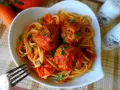 Pyszne spaghetti z klopsikami w sosie pomidorowym, posypane natką pietruszki. Idealne danie dla całej rodziny.