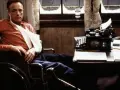 Un escritor en silla de ruedas, con un brazo en cabestrillo, mira fijamente una máquina de escribir. Escenas como esta son comunes en películas sobre escritores.