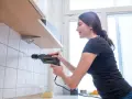 Frau bohrt mit Bohrmaschine ein Loch in die geflieste Wand, um ein Regal zu befestigen.