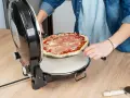 Osoba wkłada surowe ciasto na pizzę z szynką do okrągłego piekarnika.