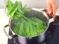 Frische zuckerschoten zubereiten: Ein Sieb mit knackigen zuckerschoten wird über einen Topf mit kochendem Wasser gehalten, um sie kurz zu blanchieren.