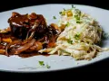 Mięso w sosie z cebulą i grzybami, przypominającymi podgrzybki, podane z kremowym makaronem posypanym parmezanem i kiełkami.