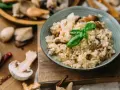 Miseczka kremowego risotto z grzybami i bazylią, otoczona świeżymi grzybami i przyprawami.