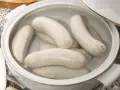 Biała kiełbasa w garnku z wodą, gotowa do parzenia. Delikatne kiełbaski czekają na idealny moment, by trafić na stół.