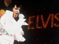 Elvis Presley singt in seinem berühmten weißen Anzug in Las Vegas, während sein Name in roten Lichtern erstrahlt.