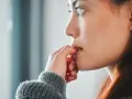Une jeune femme songeuse, les doigts près de la bouche, réfléchit à comment arrêter de se ronger les ongles.