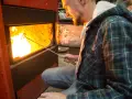 Uomo con camicia a quadri verde accende un fuoco in uno scaldabagno a legna, mostrando come funziona.