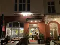 Abendstimmung vor der Pizzeria "Due Forni". Ein Mann steht im Eingangsbereich, während Gäste an Tischen im Freien sitzen.