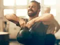 Un homme souriant effectue un exercice kettlebell, concentré sur son entraînement.