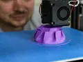 A man watches his 3D printer create a purple object, showcasing its precise 3D printer specifications in action.