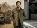 Un uomo indossa una field jacket, un capo iconico che unisce stile militare e moderno. Sullo sfondo, un campo militare con tende e jeep.