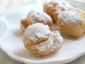 Vier goldbraune rheinische Krapfen, bestäubt mit Puderzucker, liegen auf einem weißen Teller.