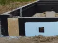 Fundament z czarną izolacją przeciwwilgociową i płytami XPS. Widać zbrojenie i fragmenty szalunku. Dobra jaka izolacja na fundament.