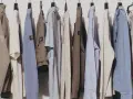 Una fila di abiti casual da uomo, con un'estetica che richiama il significato di moda evergreen: giacche, maglioni e pantaloni in tonalità neutre.