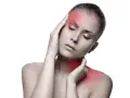 Femme souffrant de douleurs cervicales et maux de tête, mains sur la tempe et le cou, zones rouges indiquant la douleur.