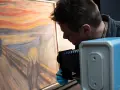 En man med blå handskar fotograferar "Skriet". Vem har målat skriet? Edvard Munch.