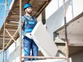 Budowlaniec w kasku na rusztowaniu trzyma płytę styropianu do ocieplenia domu.