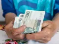 Dłonie starszej osoby trzymają banknoty 100 zł. To może być ta długo wyczekiwana 14 emerytura.