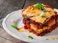 Una fetta di parmigiana di melanzane al forno, stratificata con melanzane, sugo e formaggio filante, guarnita con basilico fresco.