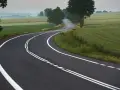 Zakręt drogi z podwójną ciągłą linią, otoczony polami i drzewami. Kierowca rozważa wyprzedzanie na podwójnej ciągłej.