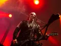Un musicien au visage peint, jouant de la basse sur scène, baigné de lumières rouges. Sa posture exprime une vie d'agonie.