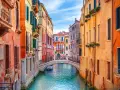 Canale veneziano con palazzi colorati e un ponte. Si immagina come fu costruita Venezia, su palafitte e ingegno.
