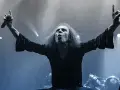 Ronnie Dio mit erhobenen Armen und Mikrofon, die Hand zum "Rock on"-Gruß geformt.