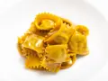 Un mucchietto di ravioli del plin, dorati e conditi con un sugo cremoso, su un piatto bianco.