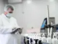 Pracownik w białym fartuchu i masce kontroluje linię produkcyjną z buteleczkami zawierającymi składnik phenoxyethanol.