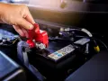 Mano che solleva il coperchio rosso di protezione del polo della batteria, un passo fondamentale per imparare come cambiare la batteria della macchina.
